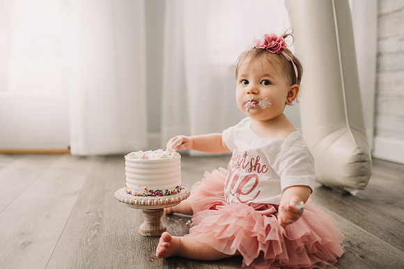 one year old eating cake during her birthday milestone session