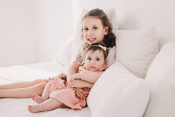 Sister snuggle on a bed siting photo session with monica carlson