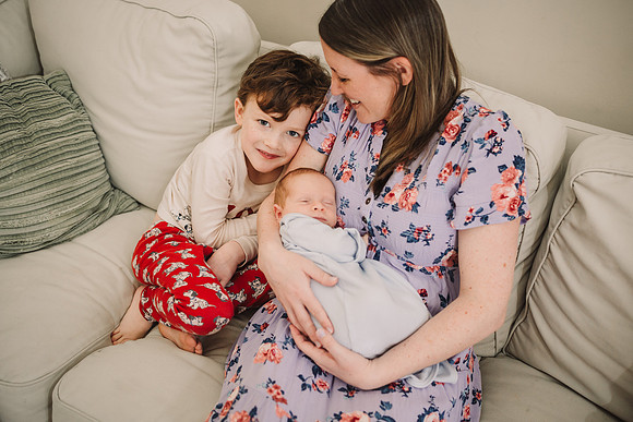 Elementary age boy snuggles with mom and new baby brother