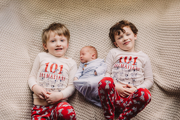 two young boys lay on either side of newborn brother