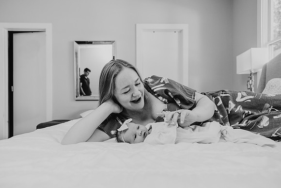 Mother lays on bed with her baby while dad watches them