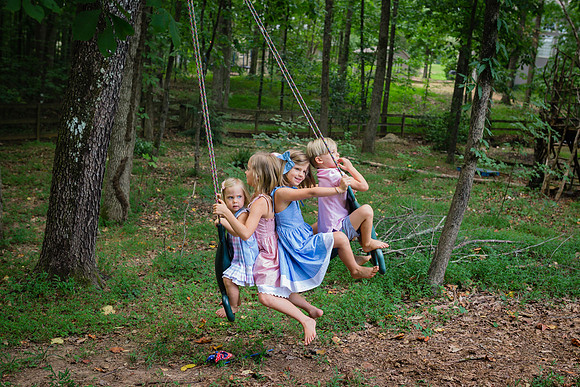 four blonde siblings riding a swing in their back yard