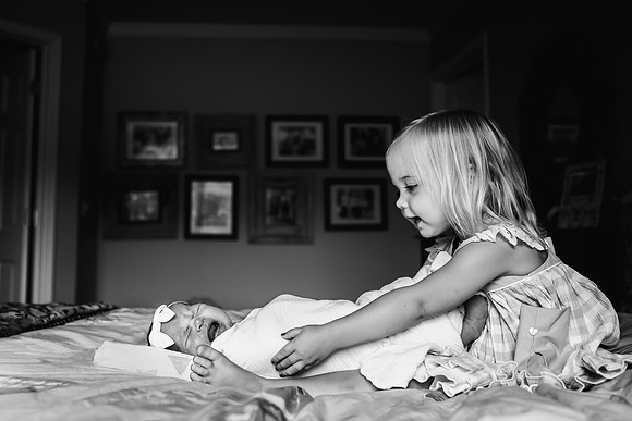 little girl consoling her newborn sister on a bed at home