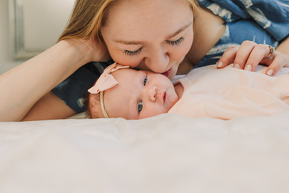 close up image of a mother kisses her newborn baby while laying down