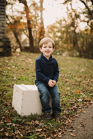 three year old boy smiles while siting on a antique block at sunset