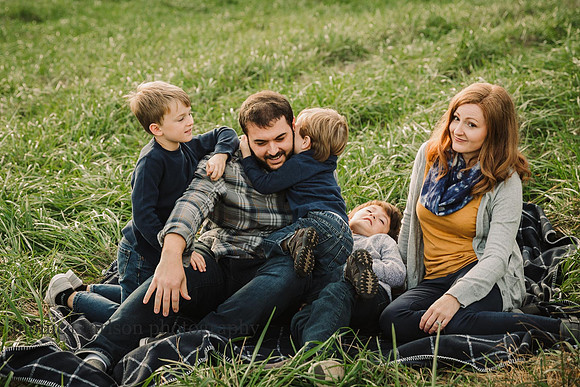 Mom makes a funny face while three sons and husband wrestle in the grass