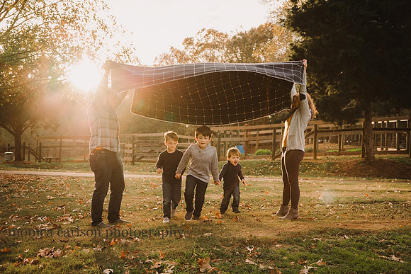 Mom and dad make a tunnel with a blanket while sons run beneath it at sunset