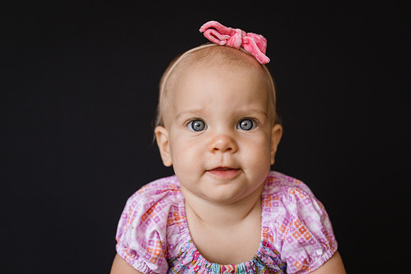 Baby sits in front of a black back drop for a portrait
