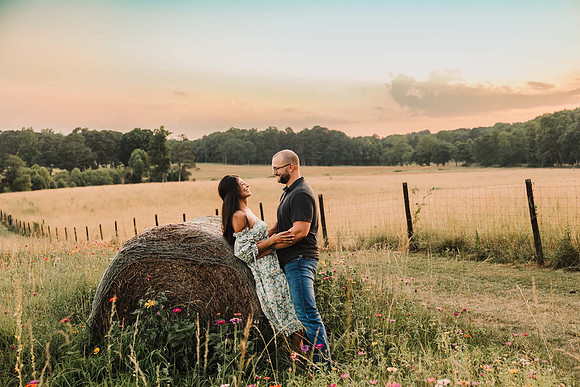 Woman and man lean against a haybale at sunset