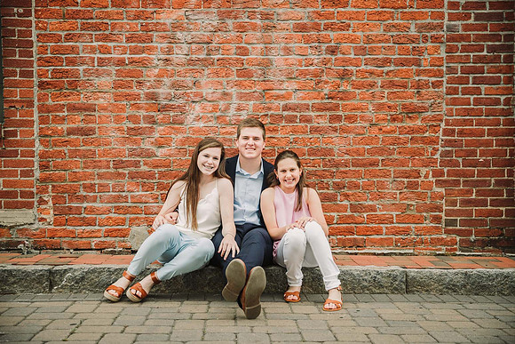 portrait of three teen siblings seated in front of brick building for a family photo session