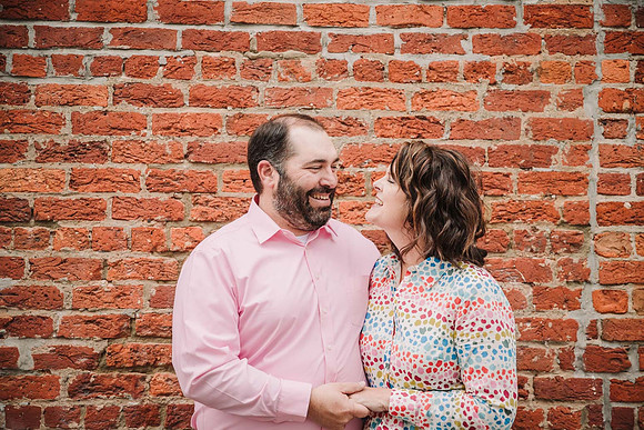 husband and wife laugh together during a family photo session with monica carlson