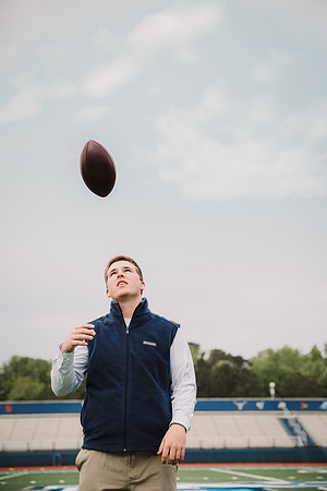 senior boy tossing a footbal at his schools stadium during his senior photo session