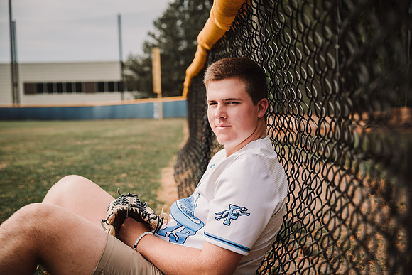 senior portrait of a boy leaning against the fence at Pope High school in Marietta, GA