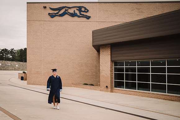 senior boy walking while in his cap and gown at Pope High school in marietta, ga