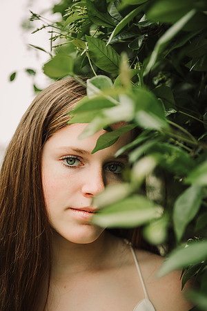 Dramatic portrait of a girl with half of her face behind leaves by monica carlson photography