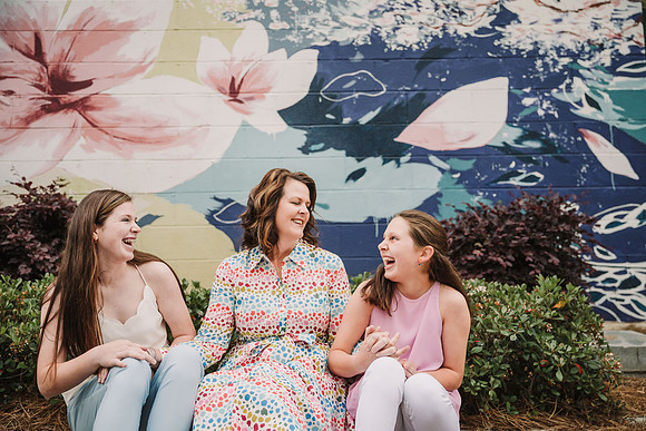 mother laughing with her teen girls in front of a mural in marietta square by monica carlson