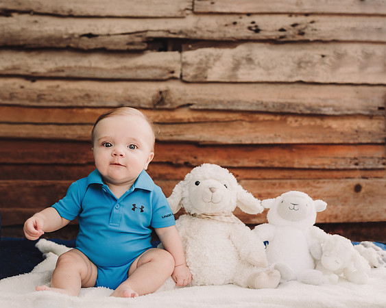 Baby boy with his lamb lovies in front of a wooden building