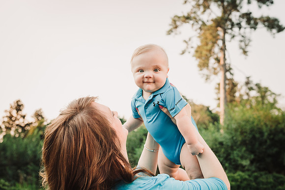 smiling baby looking directly at the camera while being held up by his mother
