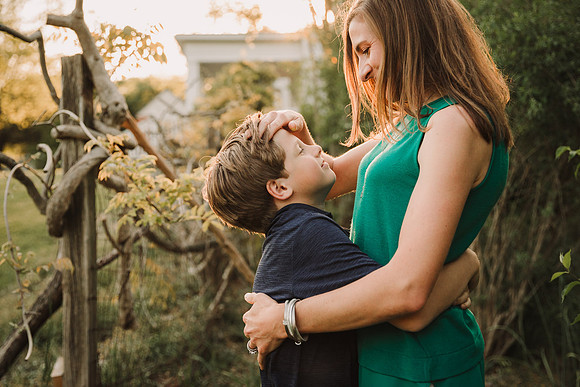 Back lit image of a mother pushes the hair from her sons face in a garden in Roswell by monica carlson