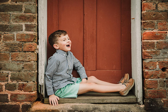 Portrait of a laughing boy in front on a red door by monica carlson