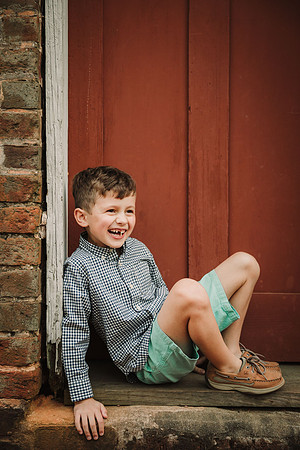 laughing elementary aged boy sitting in front of the red door on the ice house at Barrington Hall