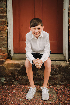 tween boy smiles for the camera while sitting in front of a red door in Roswell, GA