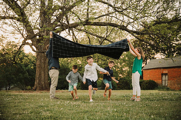 three boy brothers running under a blanket their parents are lifting up during a family photo session