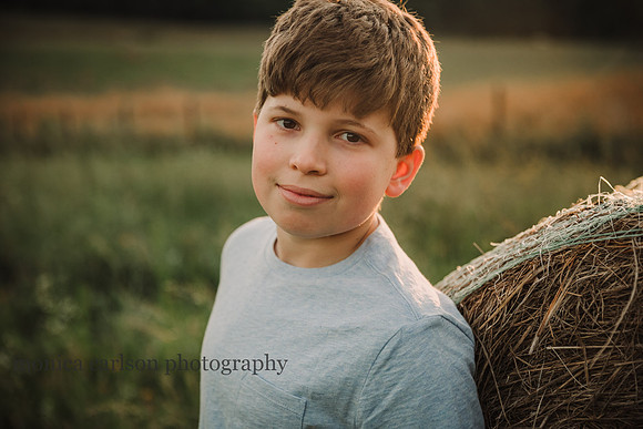 smiling teen boy leans on a bale of hay by monica carlson photography