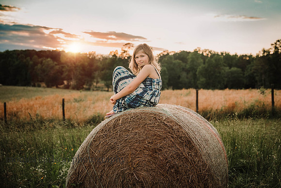 young girl smiles while siting on a haybale at sunset at Prospect farms