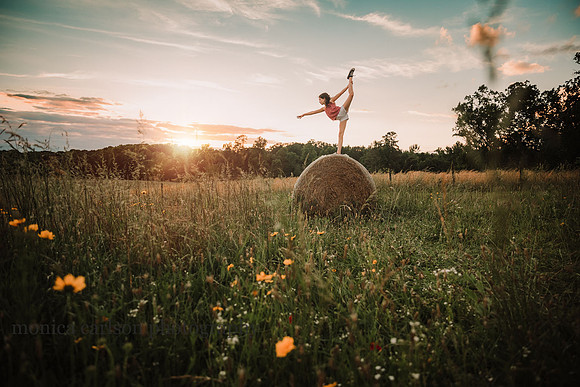 young gymnast balances a top of a hay bale in a wild flower field by monica carlson