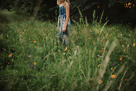 girl stands in a field on flowers at sunset