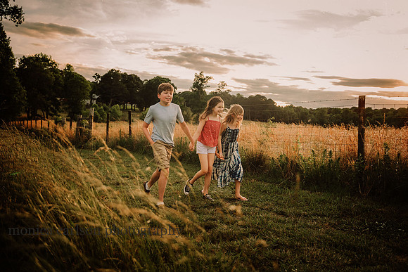 three happy kids walking together pn a farm with the sun setting behind them
