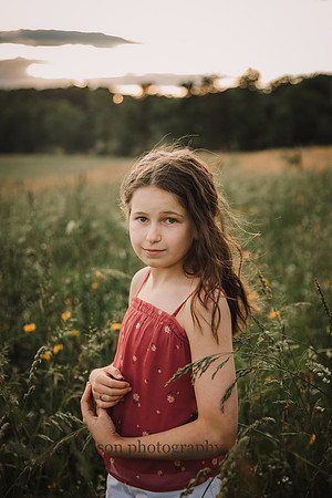 tweem girl making eye contact with the camera while stand ing in a flower field at sunset