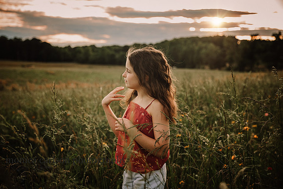 sun sets at Prospect farms while a tween girl adjusts her hair while standing on a wildflower field