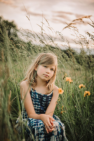 portrait of a serious blonde girl sitting on a wild flower field