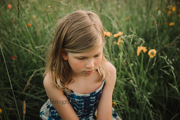 blonde girl looking down while sitting in a wildflower field in Lawernceville