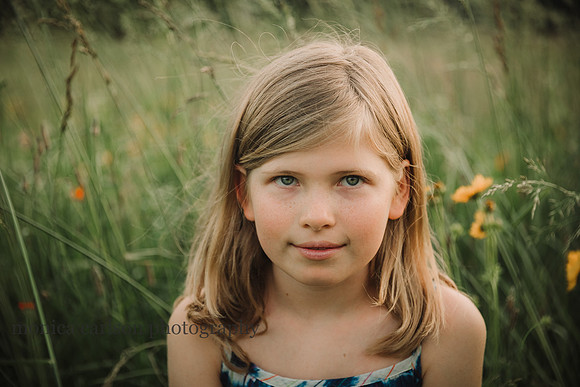 portrait of a blue eyed blonde girl siting in a flower field