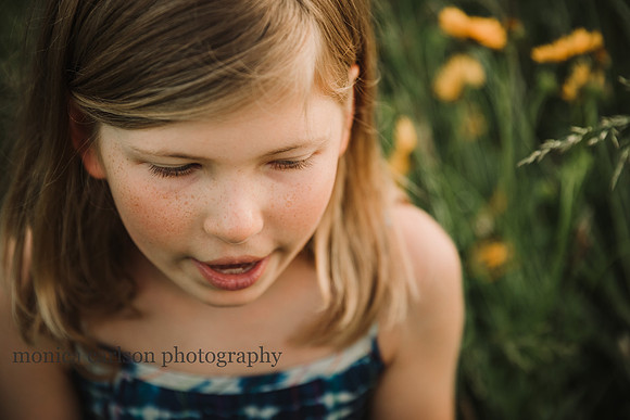 detailed image of a girls freckles and eye lashes who is sitting on a flower field