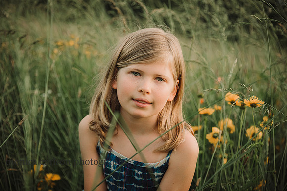 portrait of a blonde tween sitting amound a flower field