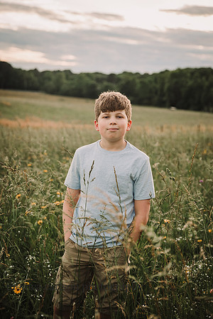 confident teen boy stand in a sunflower field at sunset by monica carlson