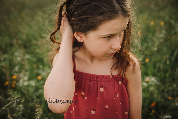 tween girl pushing her cruly brown hair away from her face while standing in a field of flowers