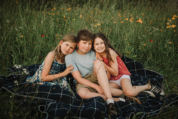 portrait of three child siblings siting on a blanket in a wildflower field on prospect farms
