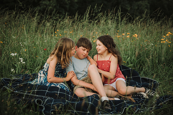 three kids laughing together while siting on a blanket in a flower field by Monica carlson