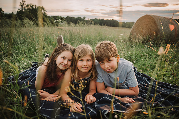 backlit image of three kids laying on a blanket in a flower field