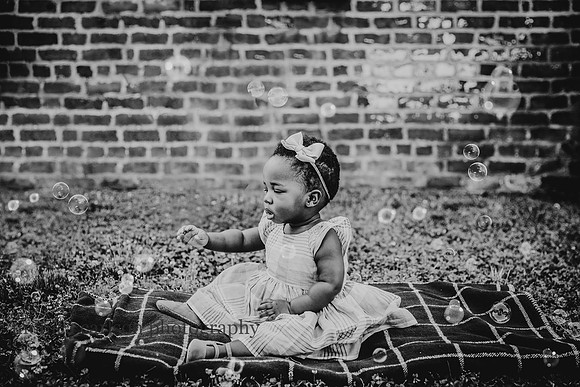 black and while image of a little girl sitting on a blanket and reaching out for bubbles by monica carlson