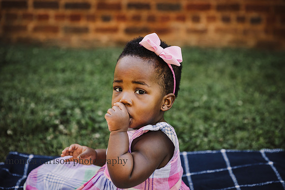 sweet, chubby cheeked one year old sucks her thumb while sitting on a blanket in front of the smoke house at Barrington hall
