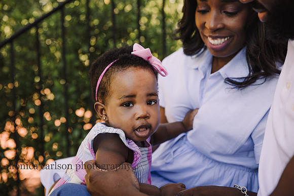 sweet, smiling one year old girl looks at the camera while sitting with her parents