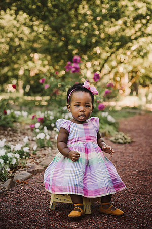 sweet one year old girl wearing a colorful dress sits on a small stool on a path outside Barrington Hall by monica carlson