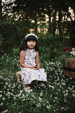 sweet little three year old girls sits for a portrait by monica carlson in a a small patch of flowers