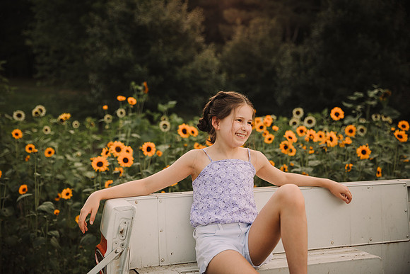 tween girl laughs in the bed of a old truck with sunflowers behind her during a photo session